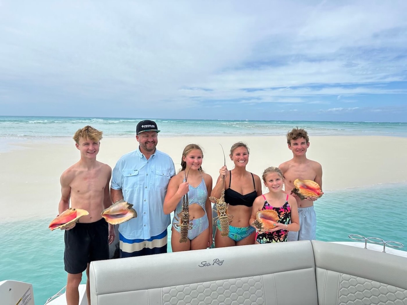 A family on a white sand beach holding up conch shells