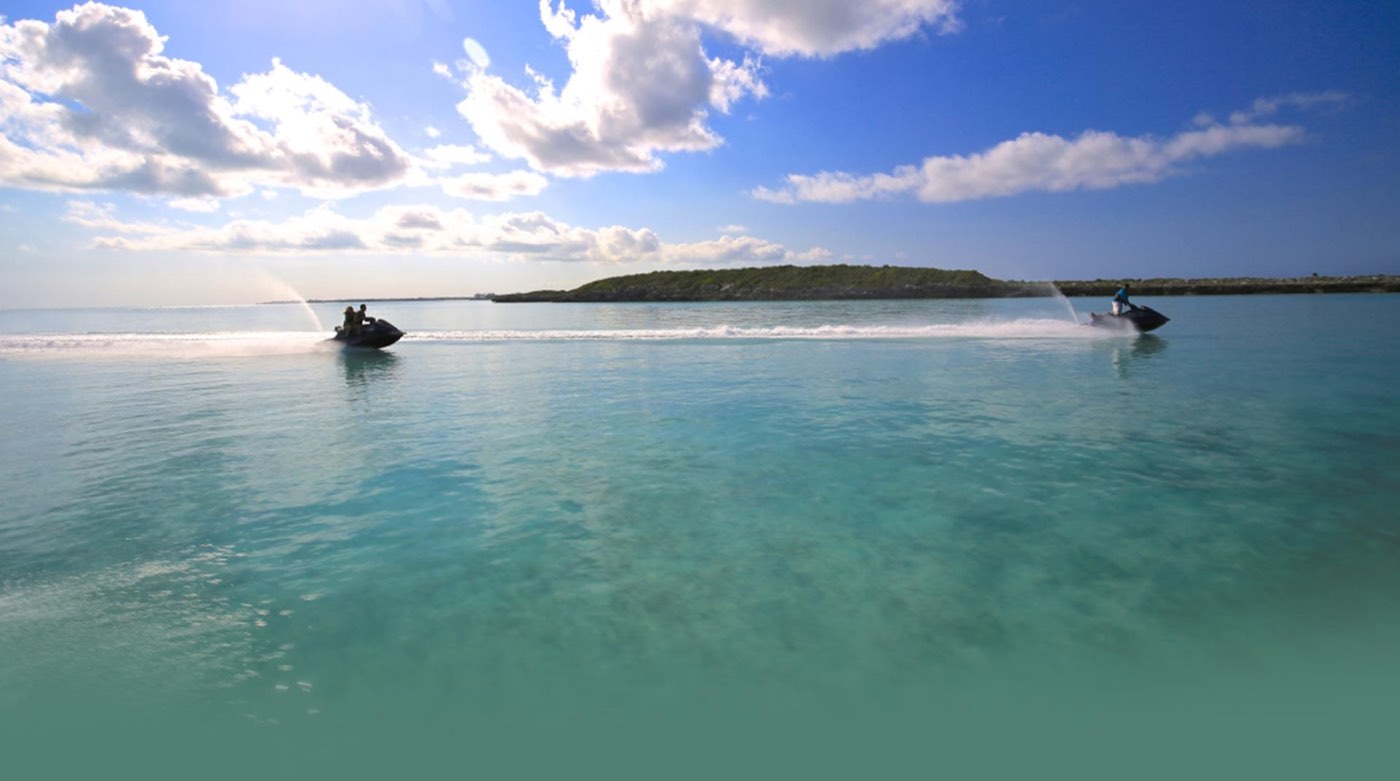 A guided group of jet skis crossing calm turquoise water toward a cay