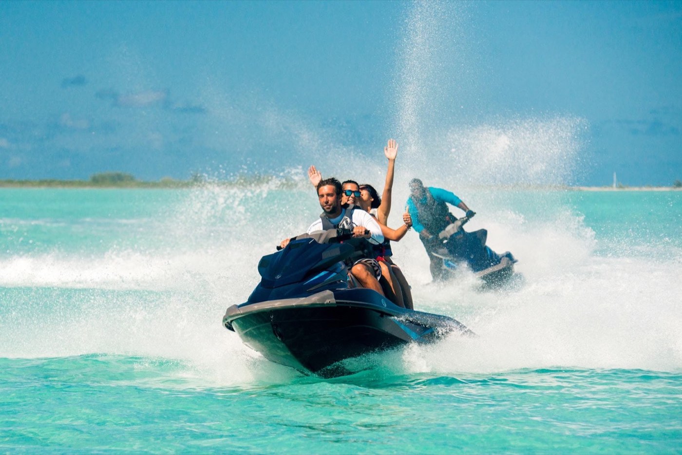 Two riders on a jet ski throwing spray across turquoise water